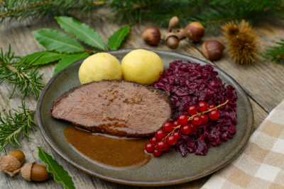 Wildschweinbraten mit Klößen und Rotkohl auf einem Teller mit herbstlicher Deko