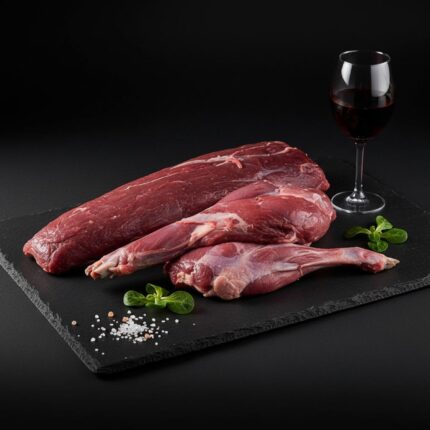 Edelteile vom Feldhasen roh, angerichtet auf einer schwarzen Schieferplatte mit grobem Meersalz, einem Glas Rotwein und Feldsalat