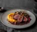 Damwildfilet mit Kürbispüree, Waldpilzen und Preiselbeer-Rotwein-Jus auf einem Teller