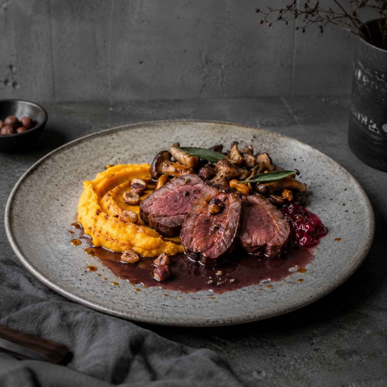 Damwildfilet mit Kürbispüree, Waldpilzen und Preiselbeer-Rotwein-Jus auf einem Teller